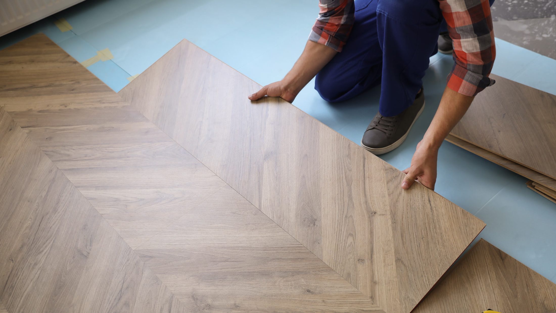 Hands carefully setting oak herringbone blocks into freshly combed adhesive